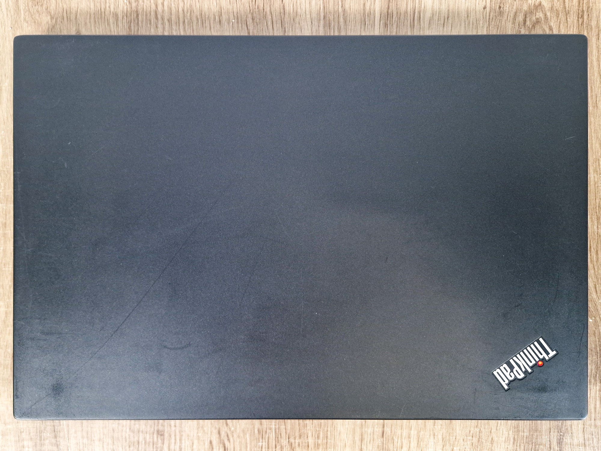 Zamknięta pokrywa laptopa ThinkPad od góry z logo, czarna obudowa z widocznymi drobnymi zarysowaniami i smugami.