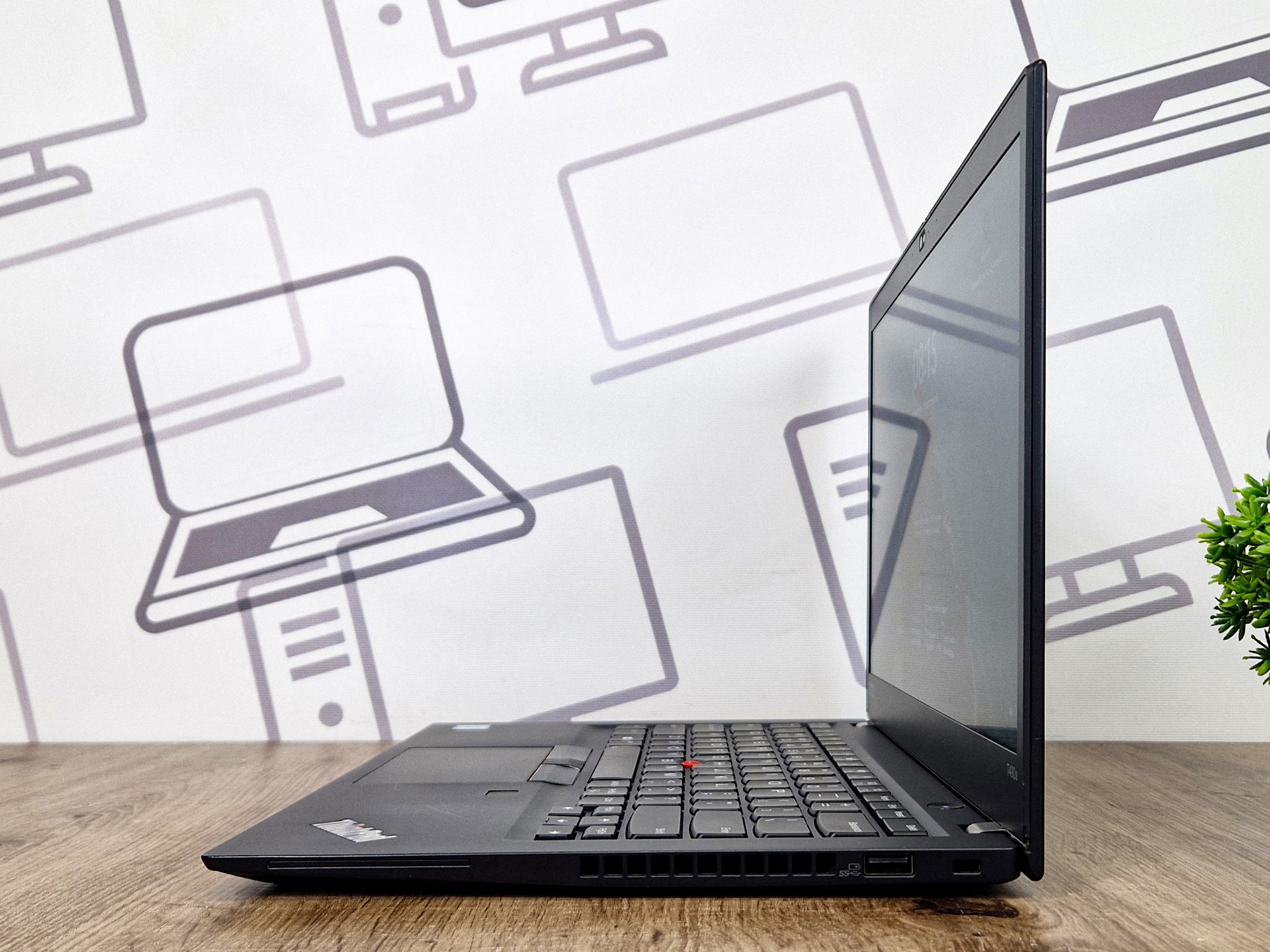 Laptop Lenovo ThinkPad uchylony pod niewielkim kątem, widok z boku na zawias, klawiaturę i logo na pokrywie.