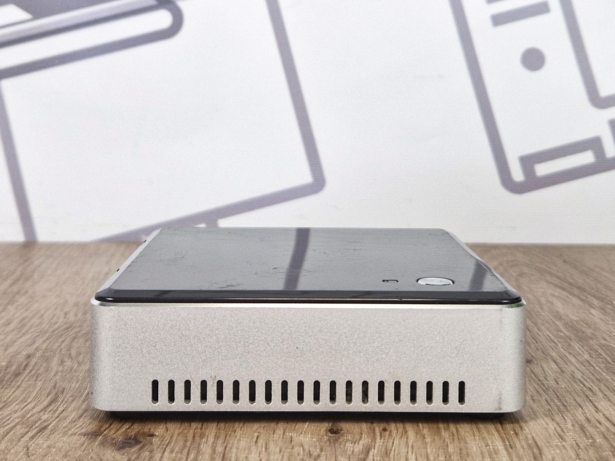 Boczny widok mini komputera Intel NUC z otworami wentylacyjnymi, srebrno-czarna obudowa, przycisk zasilania na górze.