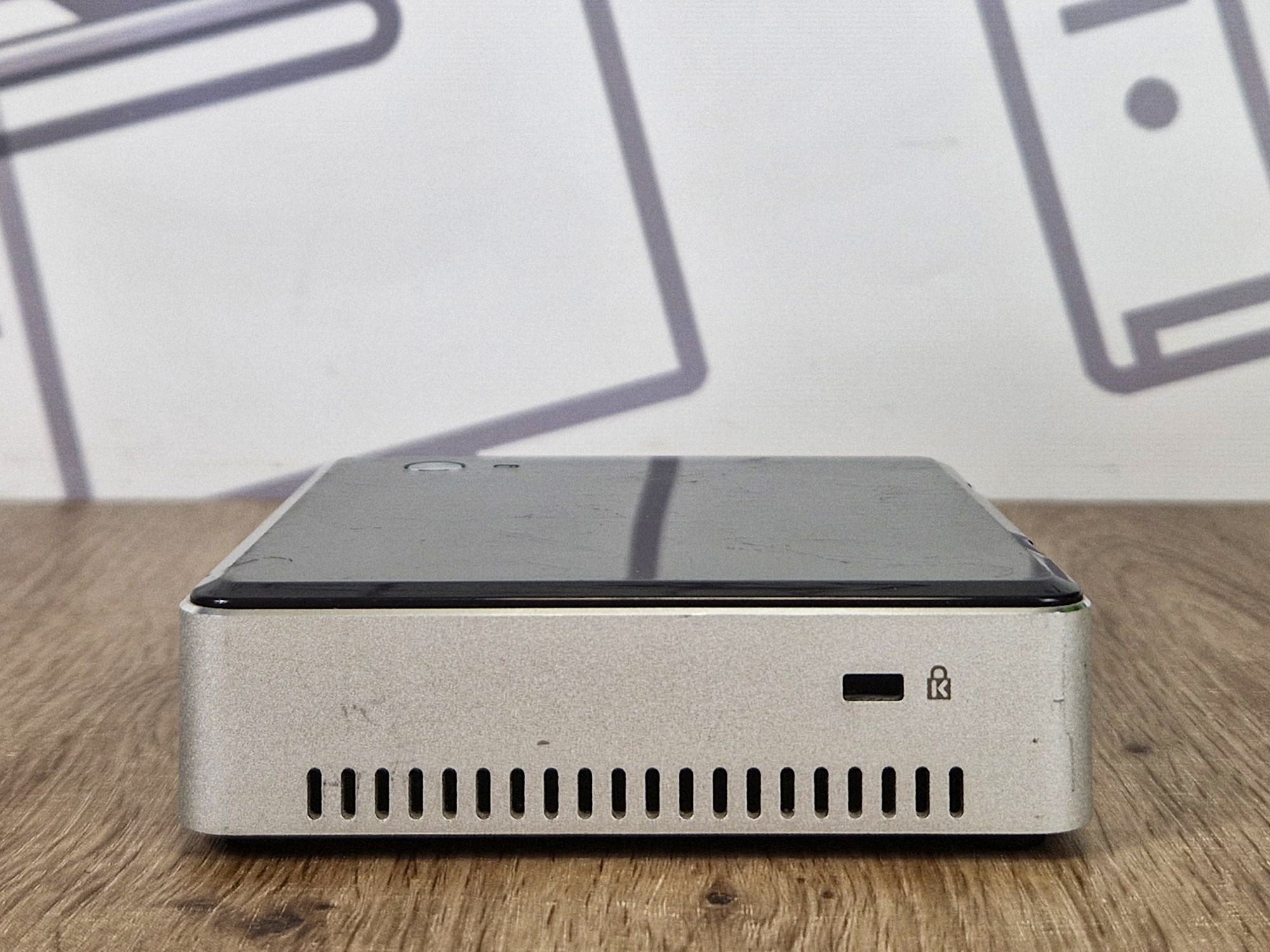 Boczny panel mini komputera Intel NUC z otworami wentylacyjnymi i gniazdem blokady Kensington, obudowa z widocznymi śladami użytkowania.