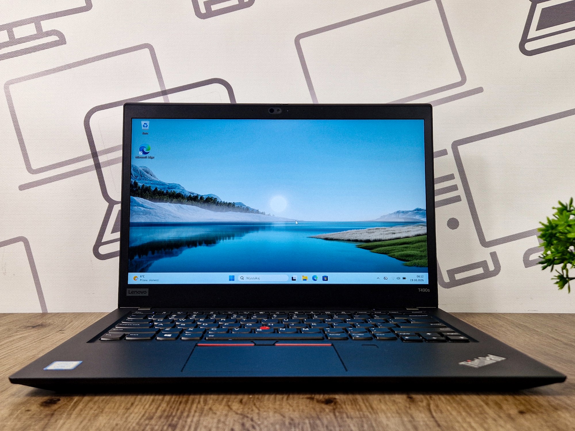 Laptop Lenovo ThinkPad otwarty pod kątem z przodu, ekran włączony z pulpitem w tle górskiego jeziora.