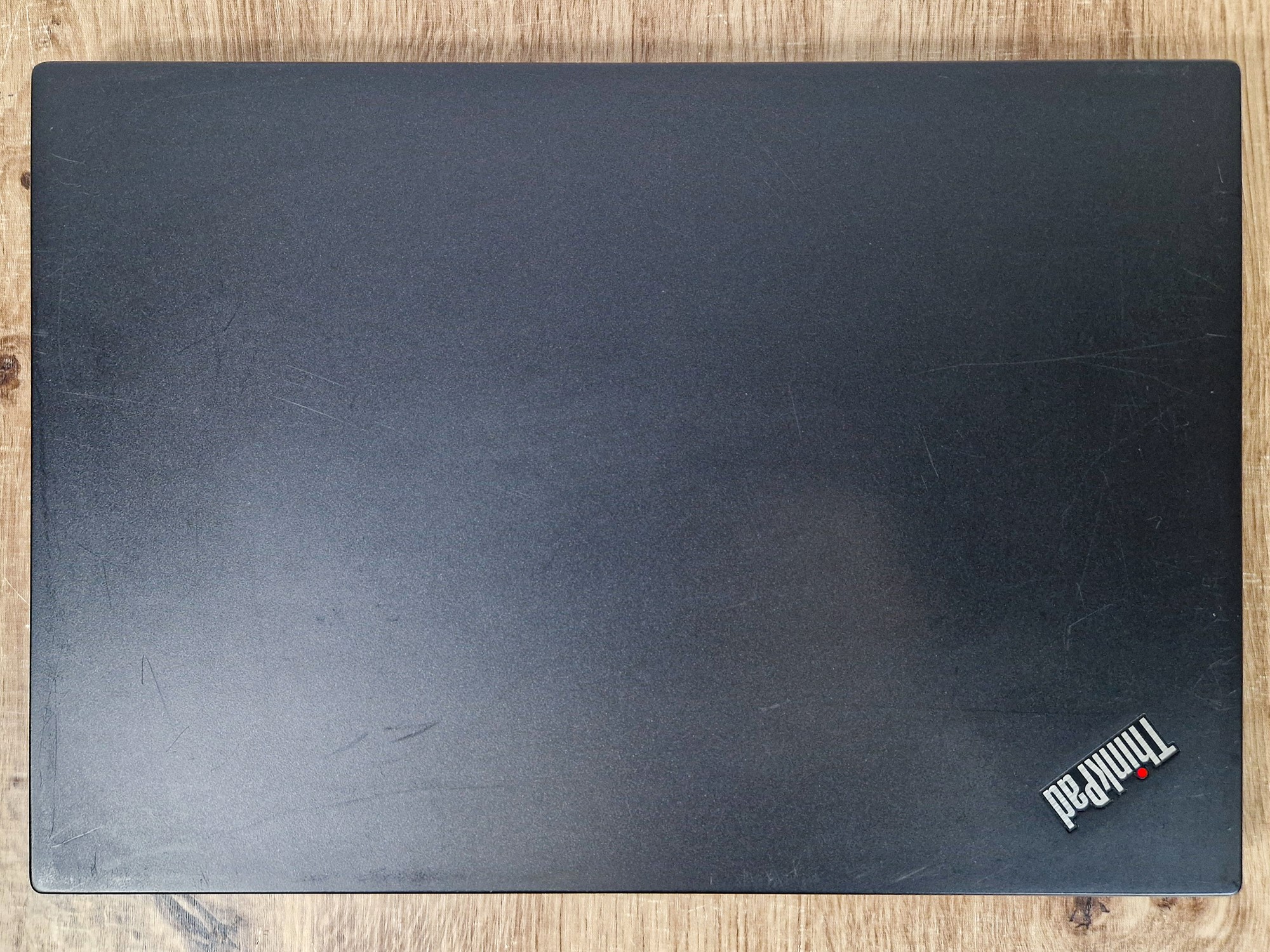 Zamknięta klapa laptopa Lenovo ThinkPad z logo w rogu, widoczne drobne zarysowania na czarnej obudowie.
